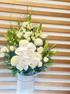 White Celebration" arrangement by Panache Flowers offers a contemporary and luxurious presentation of crisp white seasonal flowers in an elegant hatbox. It is designed to be a sophisticated and simple statement piece, suitable for all occasions from sympathy to celebrations